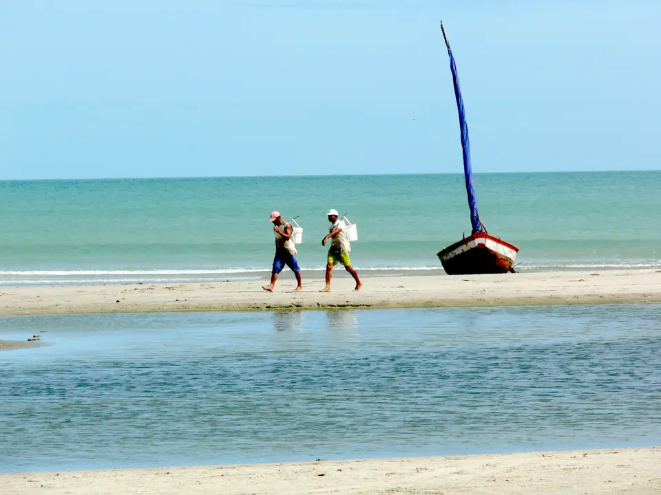 A couple of people walking along a beach next to the ocean — Jericoacoara