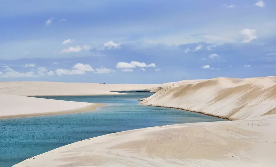 a sandy beach with a body of water in the background with Lençóis Maranhenses National Park in the background — Lençóis Maranhenses