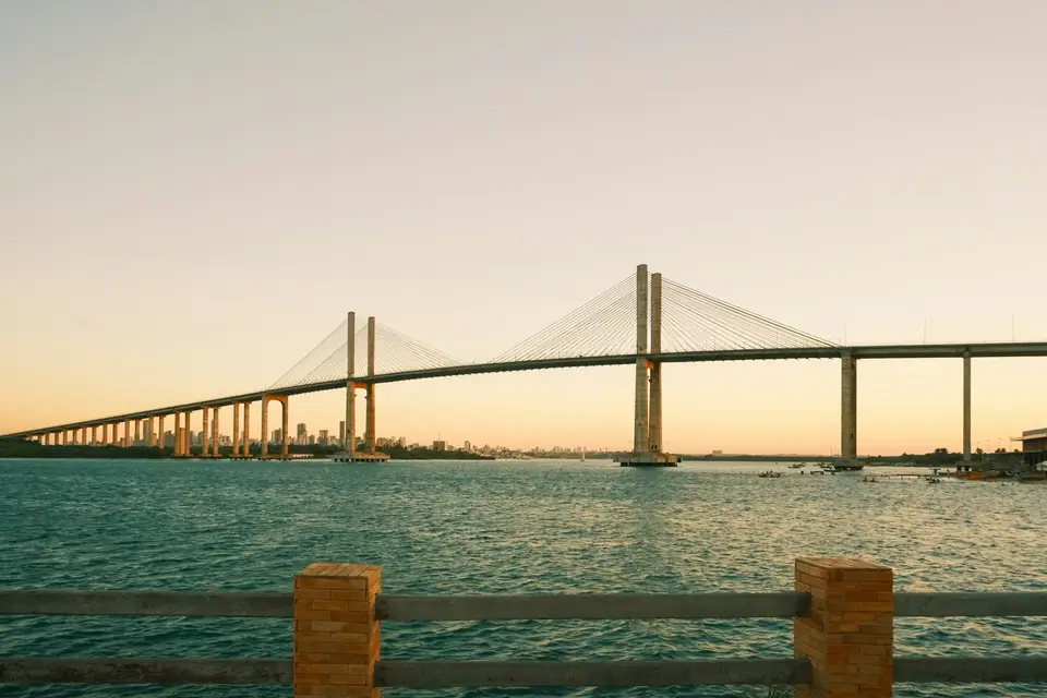A long cable-stayed bridge spanning a body of water under a pale yellow sky — Natal
