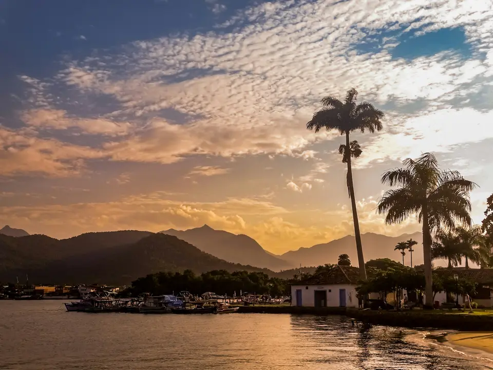 a body of water with palm trees and buildings along it — Paraty