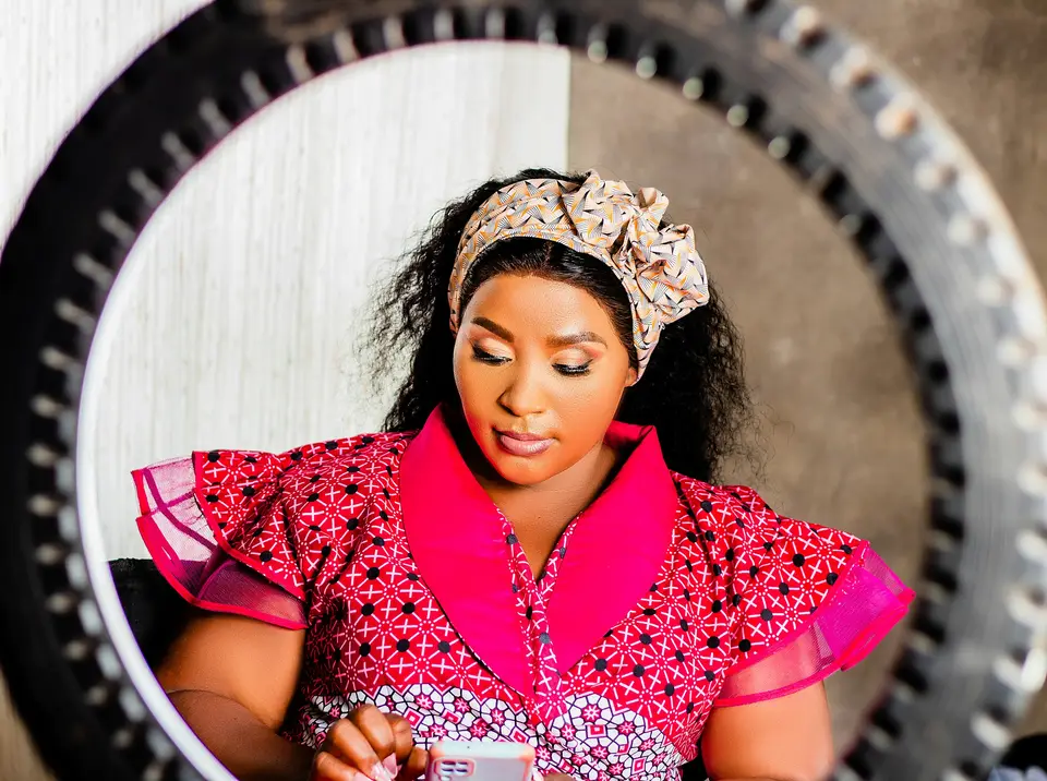A woman in a patterned pink dress and headwrap looking at her phone